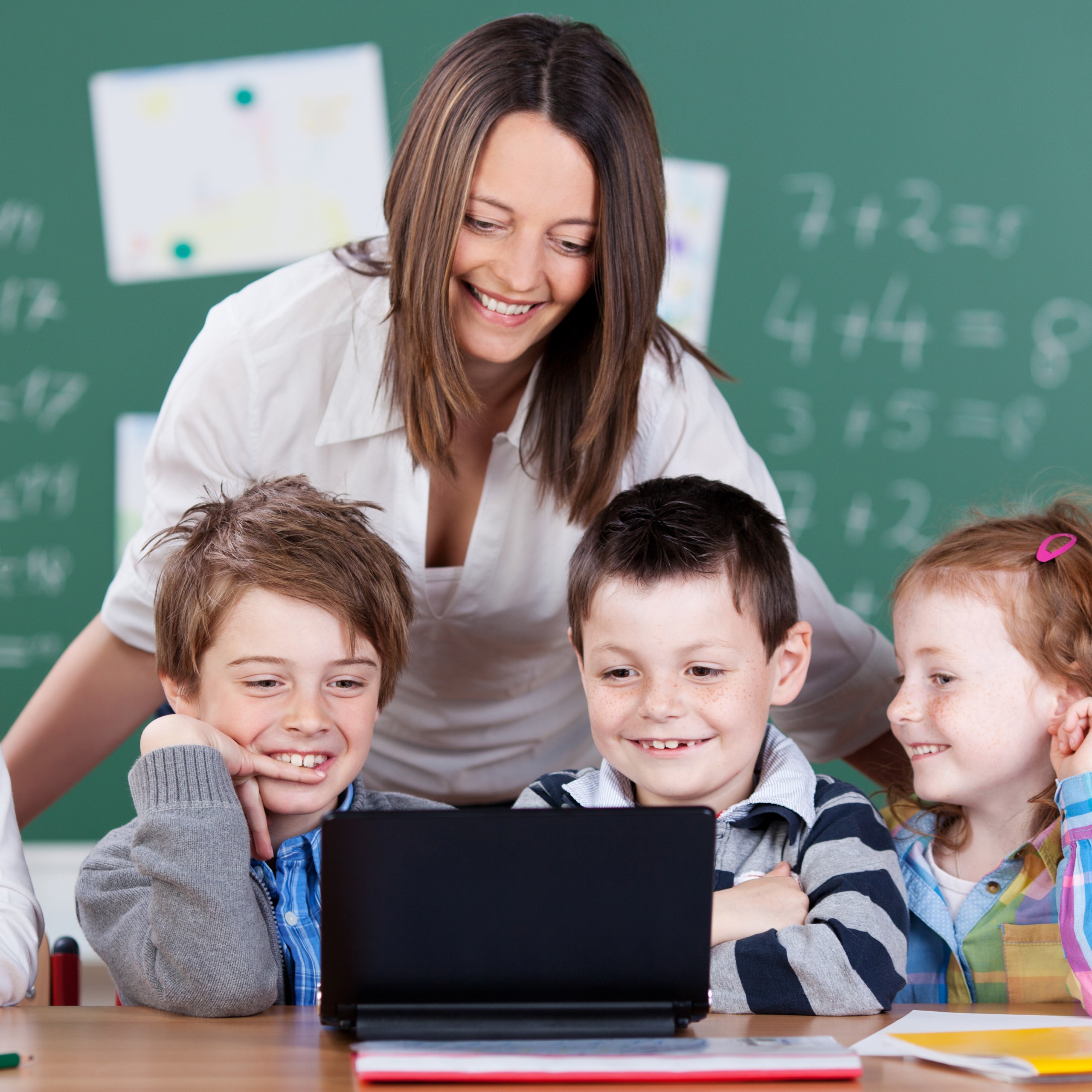 Elementary teacher supporting small group of students collaborating on laptop-based math activity